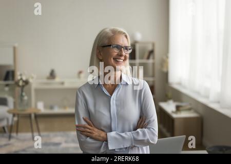 Allegra donna d'affari pensiva con occhiali in posa con braccia piegate Foto Stock