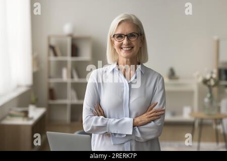 Donna d'affari anziana felice e sicura con occhiali in piedi a casa Foto Stock