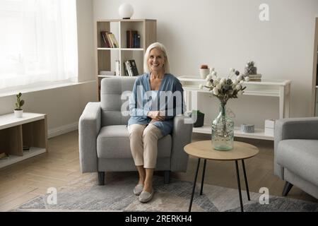 Donna anziana bionda allegra seduta informale su una comoda poltrona Foto Stock