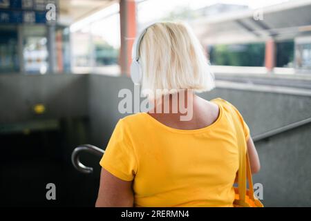 Vista posteriore della donna degli anni '50 con cuffie e una t-shirt luminosa scende fino all'attraversamento sotterraneo Foto Stock