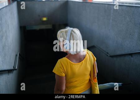 Vista posteriore della donna degli anni '50 con cuffie e una t-shirt luminosa scende fino all'attraversamento sotterraneo Foto Stock