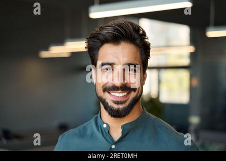 Felice giovane uomo d'affari che guarda la fotocamera in ufficio con un ritratto all'altezza della testa. Foto Stock