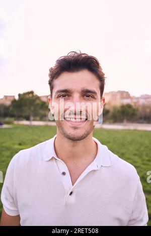 Ritratto verticale di un attraente giovane sorridente che guarda la macchina fotografica nel parco. Maschio caucasico bello Foto Stock