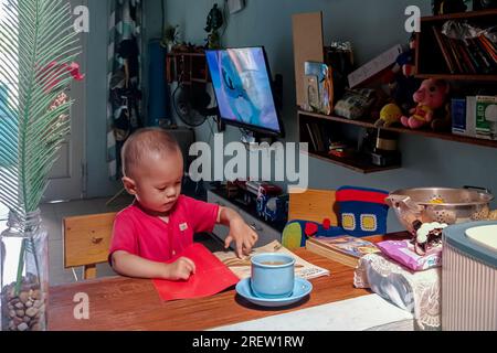 Il bambino seduto al tavolo e guardava a un libro fotografico. Un giorno in salotto Foto Stock