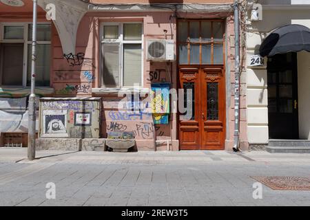 Edificio in pesca con porta marrone scuro con un'illustrazione di un uomo dall'aspetto triste sulla scatola esterna e graffiti. Sofia, Bulgaria. 29 luglio 2023 Foto Stock