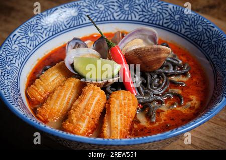 Tipico piatto di ramen caldo con brodo di pesce in una ciotola con noodle nere, calamari, peperoncini, vongole. Foto Stock
