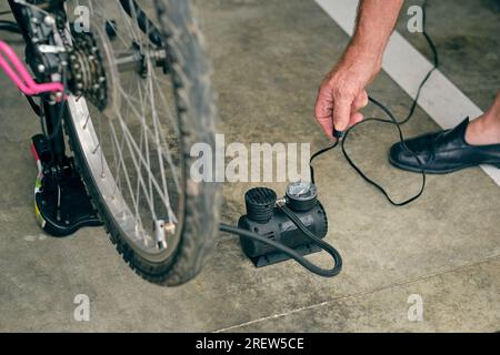 Dalla parte superiore del raccolto anonimo adulto maschio che gonfia la bicicletta con l'attrezzo elettrico con manometro Foto Stock