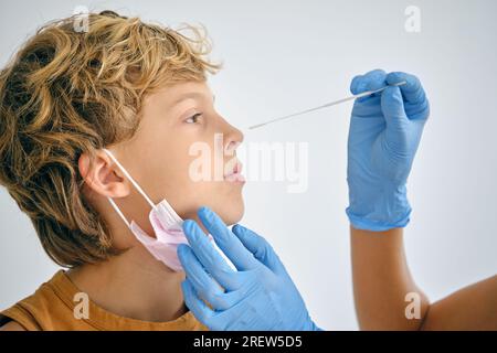Coltivare il medico anonimo in guanti monouso con un tampone che fa il test COVID 19 da Kid su sfondo chiaro Foto Stock