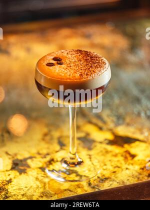 Bicchiere con cocktail alcolico espresso martini decorato con chicchi di caffè e cacao in polvere su schiuma bianca servito al bancone del bar Foto Stock