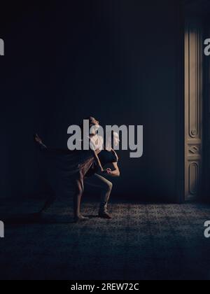 Vista laterale completa del corpo di un uomo e una donna di talento che eseguono un movimento di balletto mentre ballano insieme in uno studio buio con colonna Foto Stock