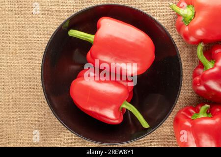 Diversi peperoni rossi dolci con piastra in ceramica nera su un panno di iuta, macro, vista dall'alto. Foto Stock