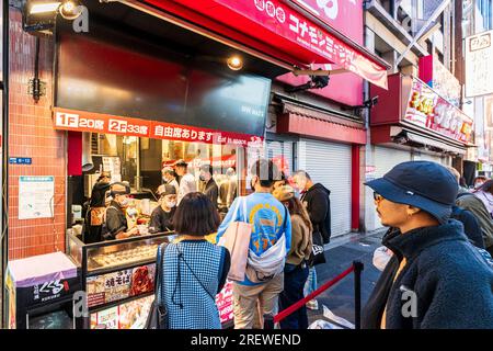 La gente fa la fila per comprare takoyaki, palline di polpo, al banco da asporto all'esterno del ristorante del Museo Konamon a Dotonbori la sera. Foto Stock