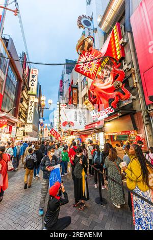 La gente fa la fila per comprare takoyaki, palline di polpo, al banco da asporto del ristorante del Museo Konamon a Dotonbori la sera. Foto Stock