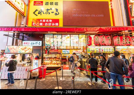 Vista notturna delle persone in coda al banco di asporto all'entrata del ristorante Creo-ru okonomiyaki e takoyaki a Dotonbori, Osaka. Foto Stock