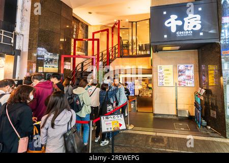 Fila di persone all'esterno dell'ingresso del ristorante Chibo okonomiyaki in attesa di tavoli all'interno. Dotonbori, il centro divertimenti di Osaka di notte. Foto Stock