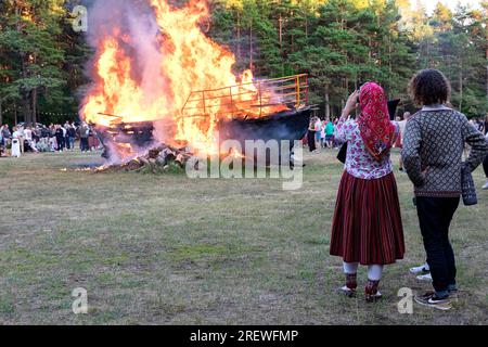 Una coppia in costumi tradizionali estoni vicino al falò delle navi in fiamme che celebrano la festa nazionale chiamata Jaanipaev sull'isola di Kihnu, Estonia Foto Stock