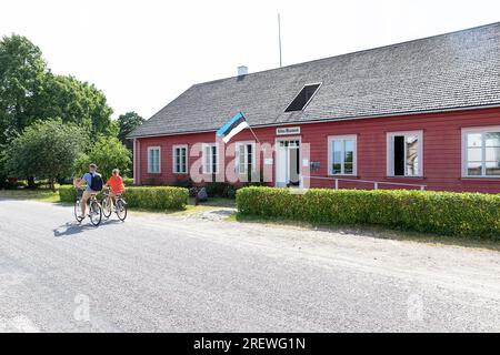 Turista, una coppia in bicicletta di fronte al museo kihnu che esplora l'isola di kihnu nel mar baltico in una splendida giornata estiva di sole, l'estonia Foto Stock