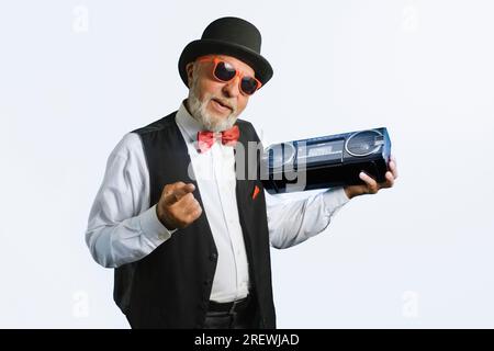 Un uomo anziano con un vecchio vestito classico, con un registratore a cassette degli anni '80 Su sfondo bianco. Foto Stock