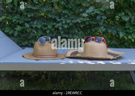 Cappelli di paglia da donna e da uomo su un lettino da spiaggia con occhiali da sole. Natura morta estiva Foto Stock