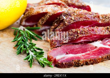 carne di manzo marinato preparata, prodotti a base di carne di maiale con strutto tagliato a fette sul tavolo con rosmarino Foto Stock