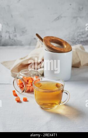 Delizioso tè nero in tazza di vetro e frutta candita su piattino giallo su sfondo chiaro Foto Stock