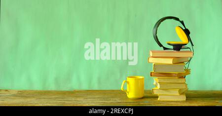 concetto di audiolibro con una pila di libri e cuffie vintage su sfondo color verde pastello, buon spazio per le copie, panoramico Foto Stock