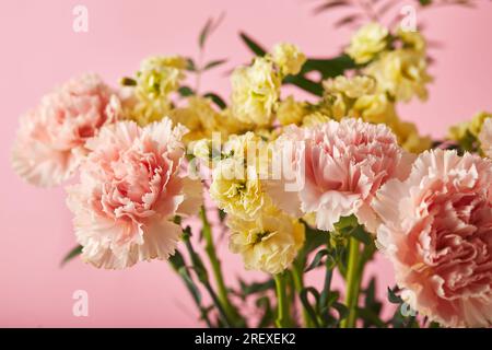 Bouquet di garofani rosa e mattiola gialla con rami verdi. Design concetto di saluto per le vacanze con bouquet di garofano su sfondo rosa. Foto Stock