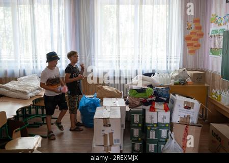 Primorskye, Ucraina. 5 luglio 2023. Ragazzi che guardano un mucchio di aiuti umanitari nella scuola del villaggio di Primorskye. Si dice che l'Ucraina abbia due eserciti - l'esercito e i volontari. Questa serie di foto documenta il lavoro congiunto di volontari ucraini e polacchi nella distribuzione di aiuti umanitari ai villaggi in prima linea nella regione di Zaporizhia: Primorsky e Stepnohirsk. Cibo, forniture per la pulizia, acqua potabile e un generatore di elettricità sono stati donati alle autorità locali. Credito: SOPA Images Limited/Alamy Live News Foto Stock