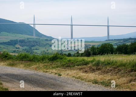 Strada sterrata con vista sul viadotto di Millau in un paesaggio rurale francese. Foto Stock