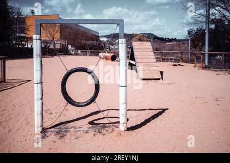 Un'area gioco per cani in contesti urbani in una giornata di sole con un'attenzione selettiva su un anello di salto sulla sabbia; uno scivolo per cani e un tubo in uno sfondo sfocato; Foto Stock