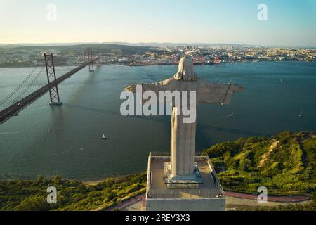 Ripresa aerea del ponte 25 de Abril che attraversa il fiume Tago che collega Lisbona e le città di Almada e il monumento cattolico del Santuario di Cristo Re Foto Stock