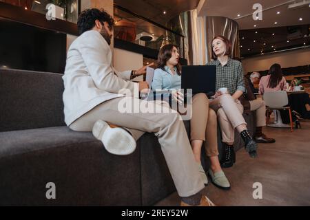 Dipendente di sesso maschile che spiega il possibile scenario alle sue colleghi mentre lavora insieme in ufficio seduto su un divano grigio Foto Stock