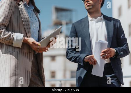 Foto ritagliata di partner commerciali maschili e femminili in possesso di documenti e tablet che discutono di lavoro mentre lavorano in remoto in città Foto Stock