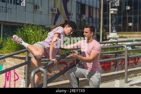 Forte atleta maschile che aiuta la sua amica a saltare su una recinzione metallica Foto Stock