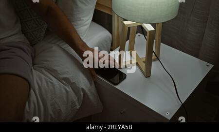 Giovane arabo che tiene lo smartphone seduto sul letto in camera da letto Foto Stock