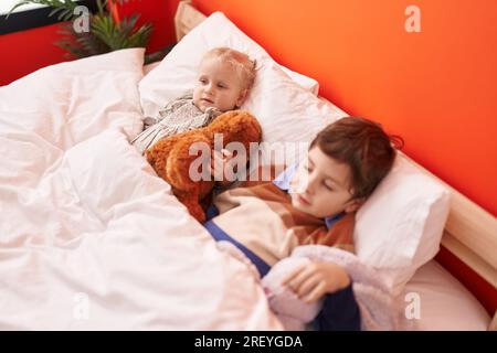 Adorabile ragazzo e ragazza che abbraccia orsacchiotto che dorme a letto in camera da letto Foto Stock