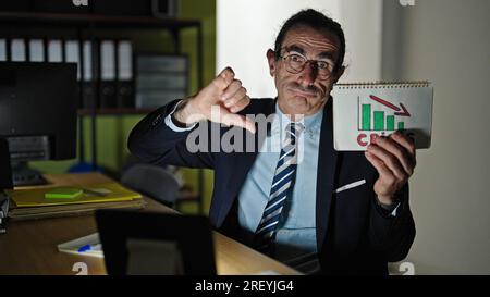 Uomo di mezza età lavoratore d'affari in possesso di un grafico di crisi che fa il pollice in ufficio Foto Stock