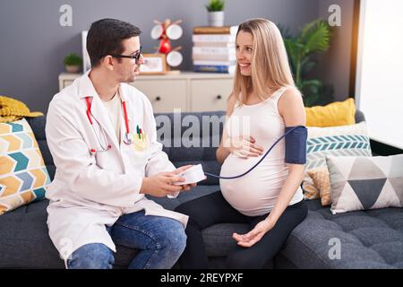 Uomo e donna medico e paziente incinta che hanno una consultazione medica utilizzando il tensiometro a casa Foto Stock