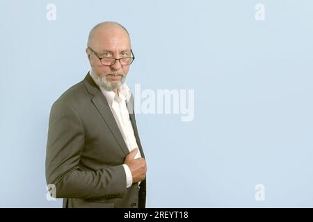 Ritratto di un uomo anziano con un classico vestito, occhiali, barba grigia. Su sfondo azzurro. copia spazio. banner Foto Stock