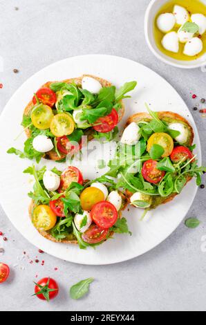 Bruschetta con pomodori ciliegini, mini mozzarella e salsa di pesto, toast caprese, gustoso spuntino Foto Stock