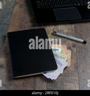 Frammento di libro contabile di un dispositivo di conto con banconote in euro e una penna stilografica sullo sfondo di un tavolo di legno. Foto Stock