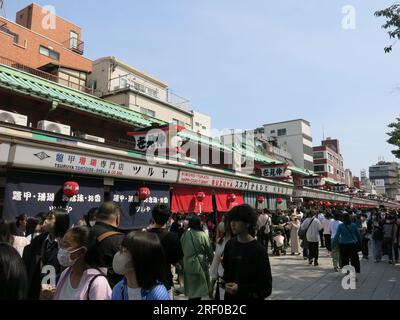 Folle di turisti e visitatori affollano le strade che circondano il Tempio senso-ji, che sono piene di bancarelle e bancarelle che vendono souvenir e dolci. Foto Stock