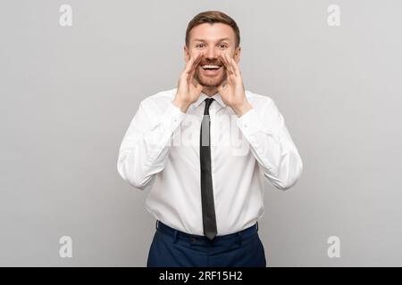 Ritratto di un lavoratore felice che urla con le mani vicino alla bocca su sfondo grigio. Banner. Foto Stock