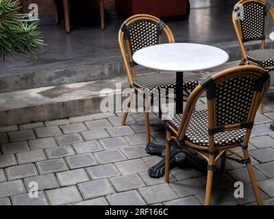 Sedie vuote e confortevoli in rattan d'epoca con tavolo rotondo in marmo decorato con pavimento in mattoni di cemento grigio all'interno dell'edificio con luce soffusa naturale Foto Stock