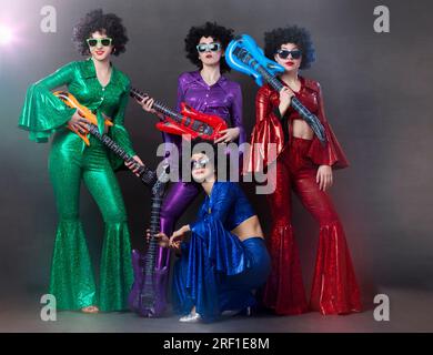 Ragazze con costumi brillanti e brillanti e parrucche con chitarre. Disco band di musica vintage per donne in stile disco. Foto Stock