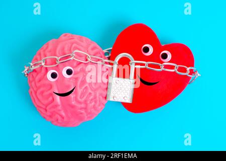 Simpatici personaggi antropomorfi del cuore e del cervello, legati strettamente da una catena e fissati con un lucchetto isolato su sfondo blu. Intelletto a Foto Stock