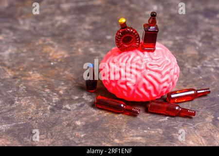 Modello in miniatura del cervello umano accompagnato da una collezione di piccole bottiglie di liquore e birra. Concetto correlato alla mente umana e al consumo di alcol. Foto Stock