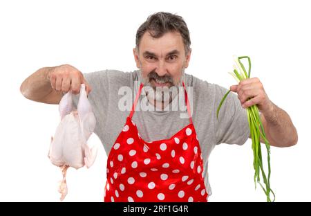 Un anziano cuoco maschio barbuto in grembiule rosso a pois contiene un pollo crudo e un mazzo di cipolle su sfondo bianco. Cuocere con il pollo. Foto Stock