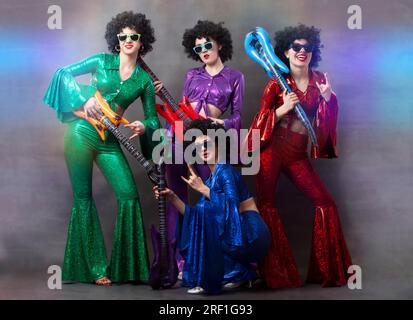 Ragazze con costumi colorati e lucenti e parrucche africane con chitarre. Disco band di musica vintage per donne. Foto Stock