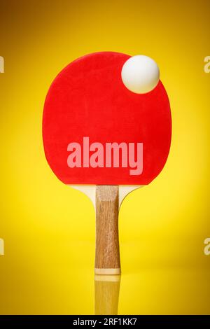 Lato rosso di una racchetta da ping pong con una palla bianca su sfondo giallo. Concetto di gara di ping pong da ping pong. Foto Stock